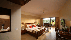 Elegant Exotica Room at Uday Suites featuring a plush bed, classic wooden furniture, warm lighting, a balcony with lush greenery, and a guest enjoying the view