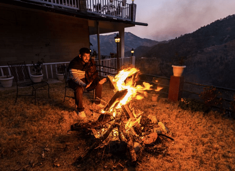 A roaring bonfire in the twilight outside of the resort, with hills visible in the distance at BluSalzz Collection - Suvaasa Resort, Ramgarh