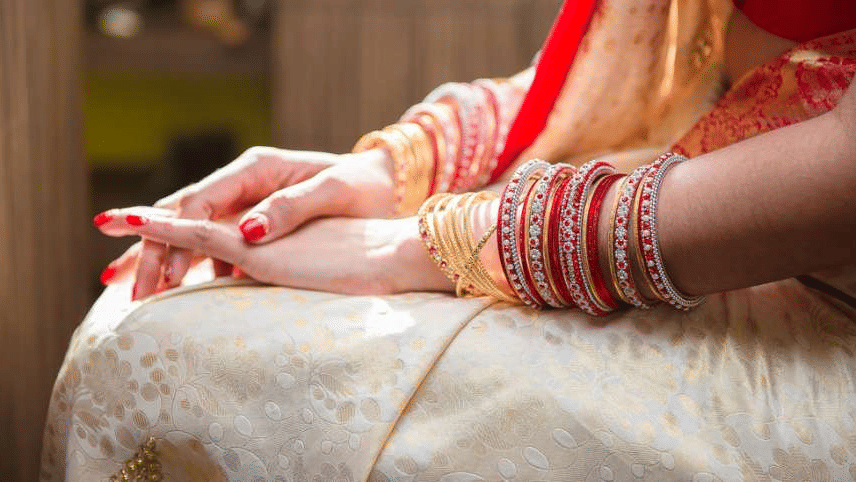 A woman sitting with folded hands and showing her bangles.