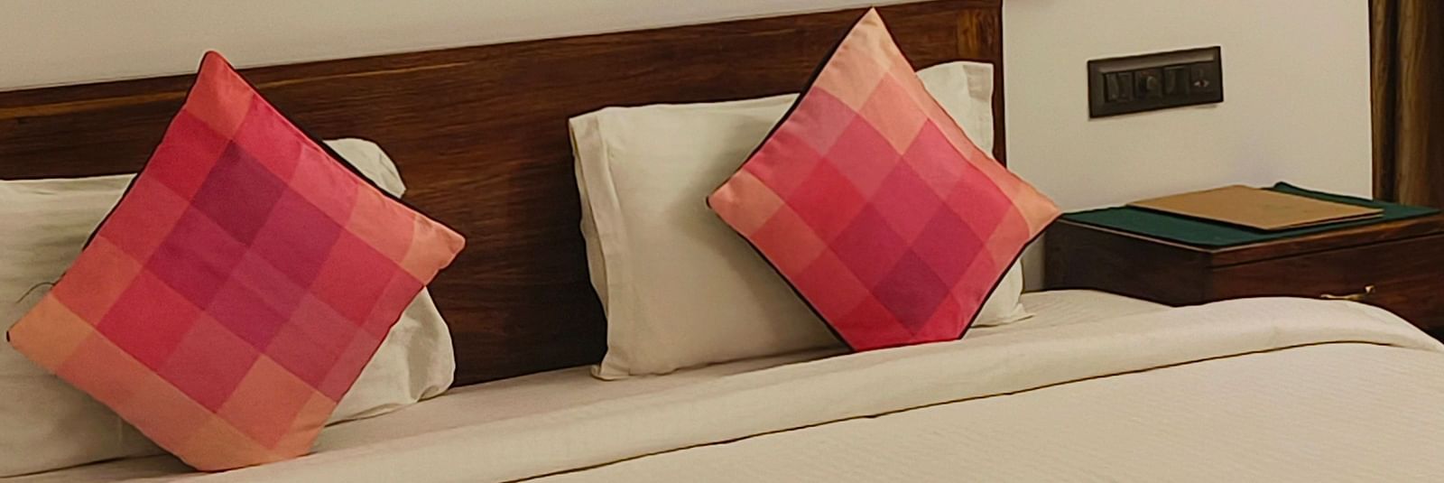 Front view of a double bed with two pink pillows kept on it and hexagonal frames hanging on the wall in 101 non-ac room at Ananda Holiday Home, Wayanad 1