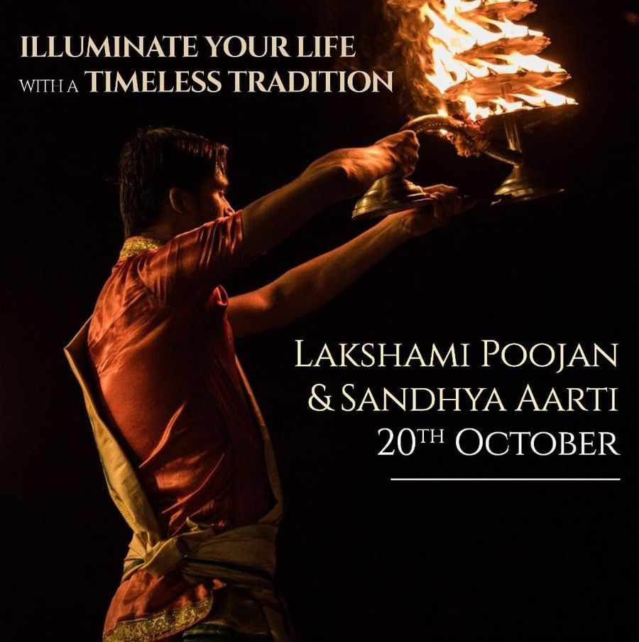 Diwali event flyer for Heritage Village Resort & Spa, Manesar, featuring a man performing Sandhya Aarti with a flaming oil lamp. Text highlights Lakshami Poojan & Aarti on 20th October, with a reservation contact number.