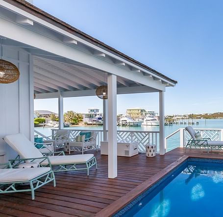 Private poolside deck with sun loungers and seating, overlooking a coastal bay with docked boats and distant hills at Abaco Inn