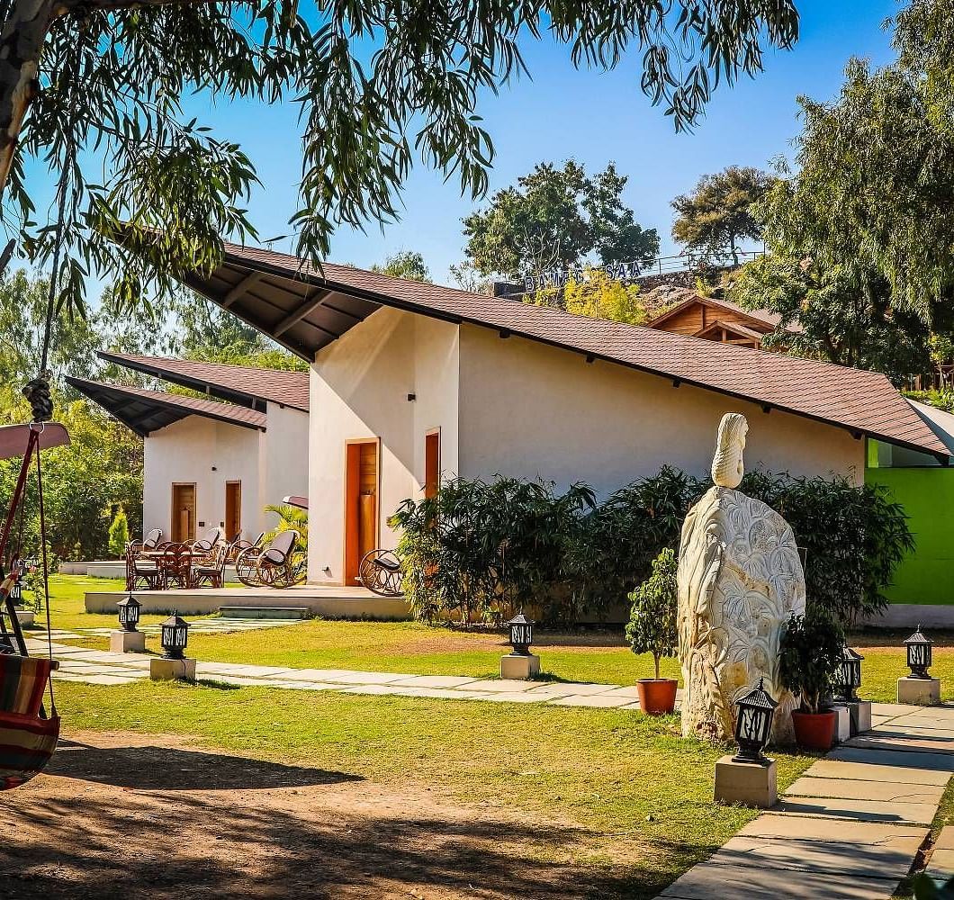 A modern building with a sloping roof sits amidst lush greenery.- Bamboo Saa Resort & Spa, Udaipur