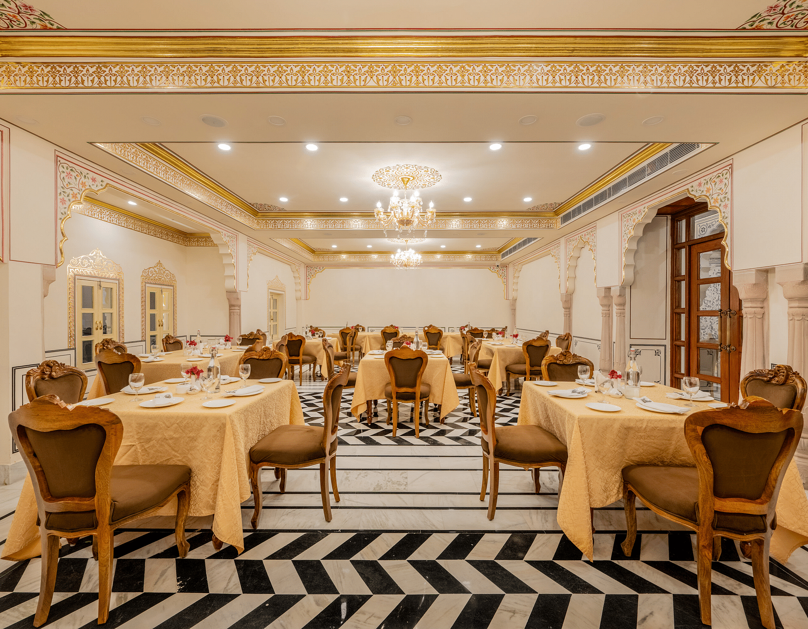 a well arrnaged dining setup in our indoor restaurant with black and white tiles and elegant furnishings - Brij Castle, Jaipur