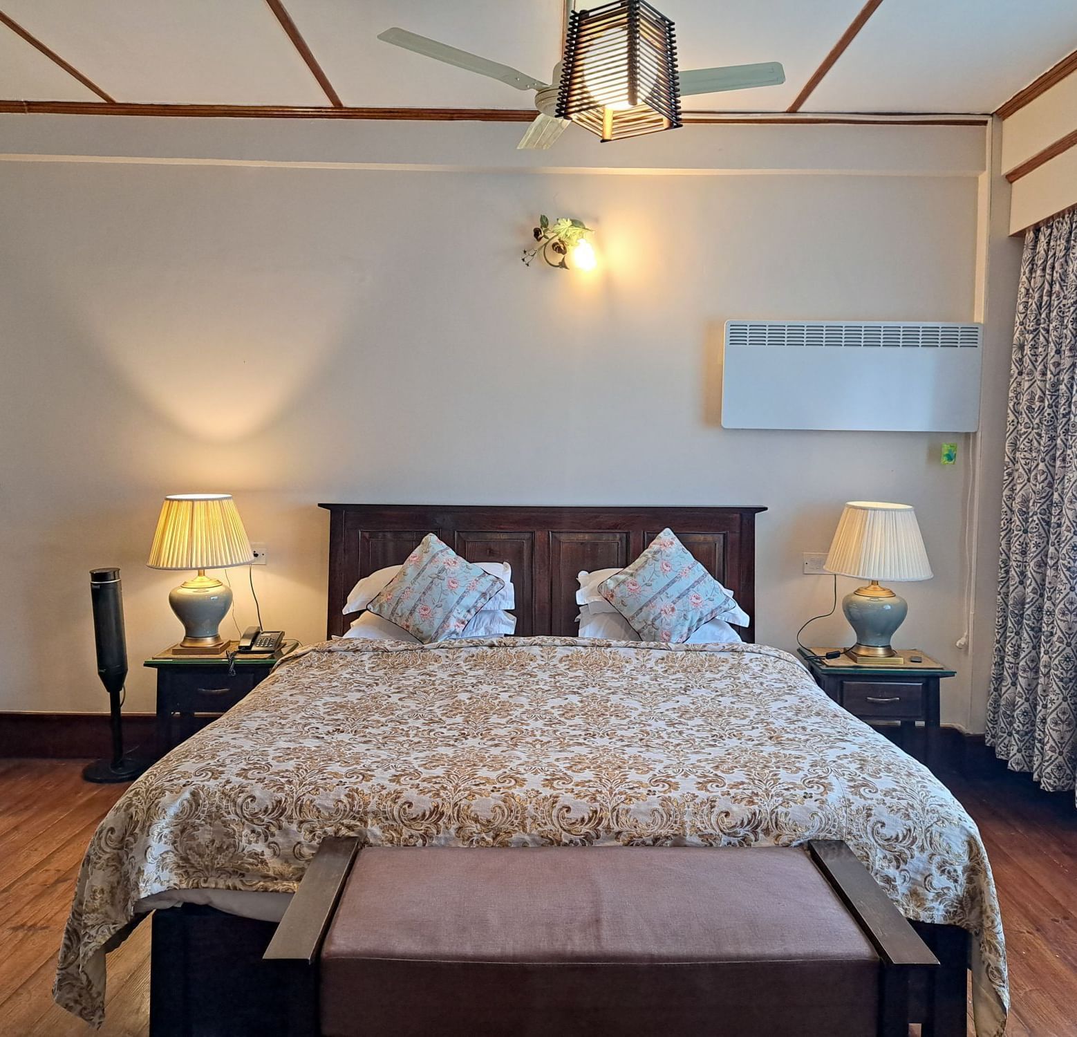 A well lit room at The Heritage Club - Tripura Castle Hotel & Spa featuring a large bed with a patterned bedspread, two bedside tables with lamps, and a ceiling fan