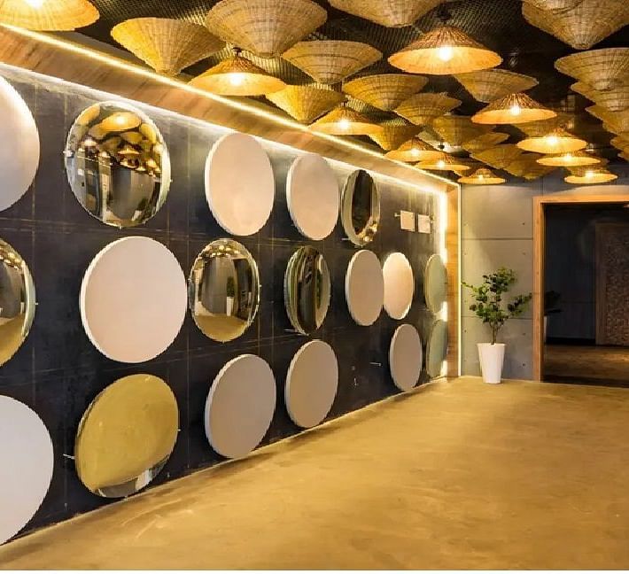 A chic entrance hallway with reflective circular wall panels, warm ambient lighting, woven ceiling décor, and potted plants for a sophisticated welcome at TGI Livancia Hillside, JC Nagar, Mysore.