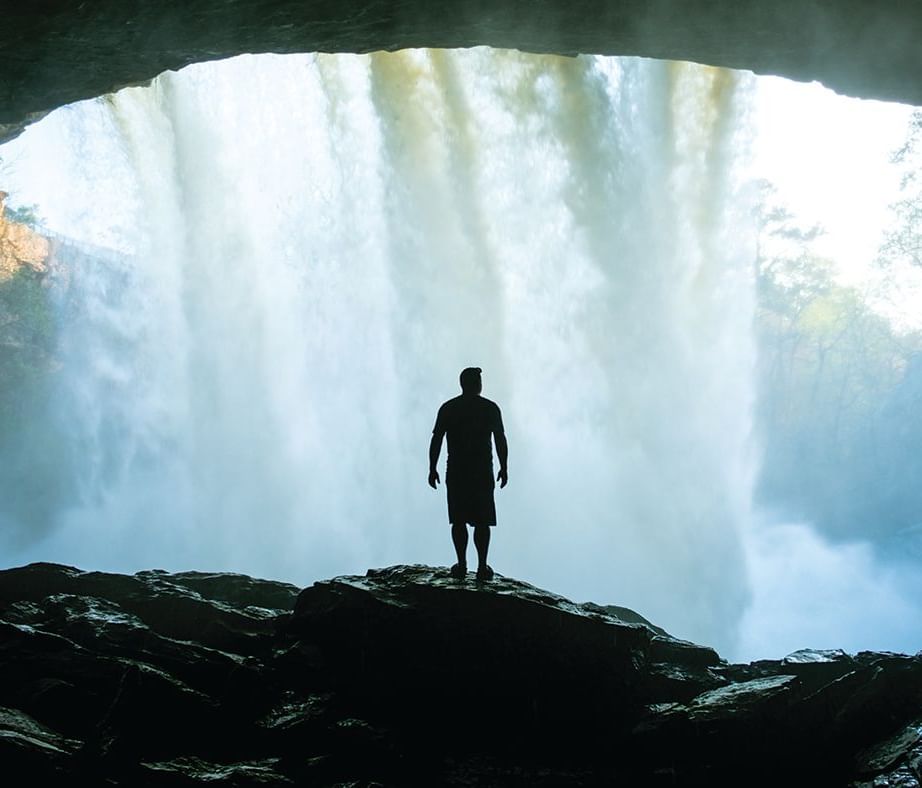 A man standing at the mouth of Siju caves with a waterfall cascading in the background - Tura Chapter Hotel by Polo