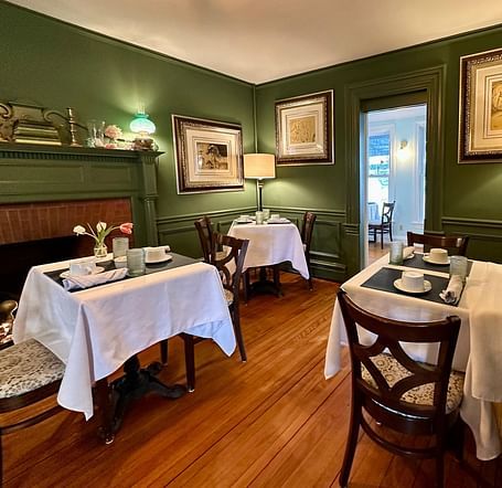 A dining room at Hartstone Inn featuring green walls, white tablecloths, and framed artwork