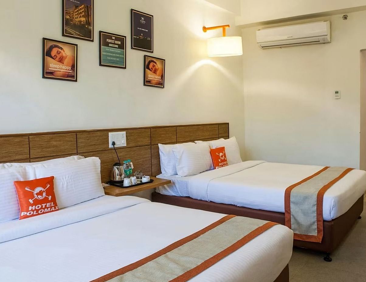 full view image of the max family room featuring two plush double beds along with a split air-conditioner and a bedside table between the two beds - Max Hotel Jabalpur