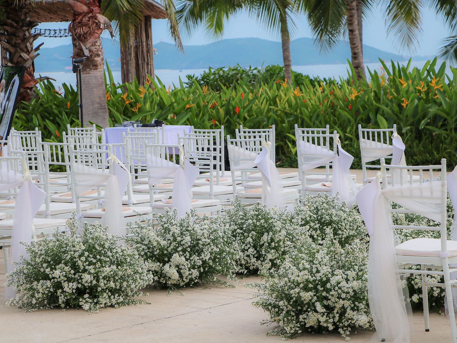 An array of white chairs with flowers placed by the side of the chairs - Alibu Resort Nha Trang
