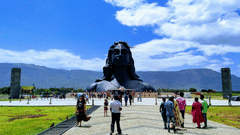 Visitors walking along a wide pathway towards the Adiyogi statue under a bright blue sky.