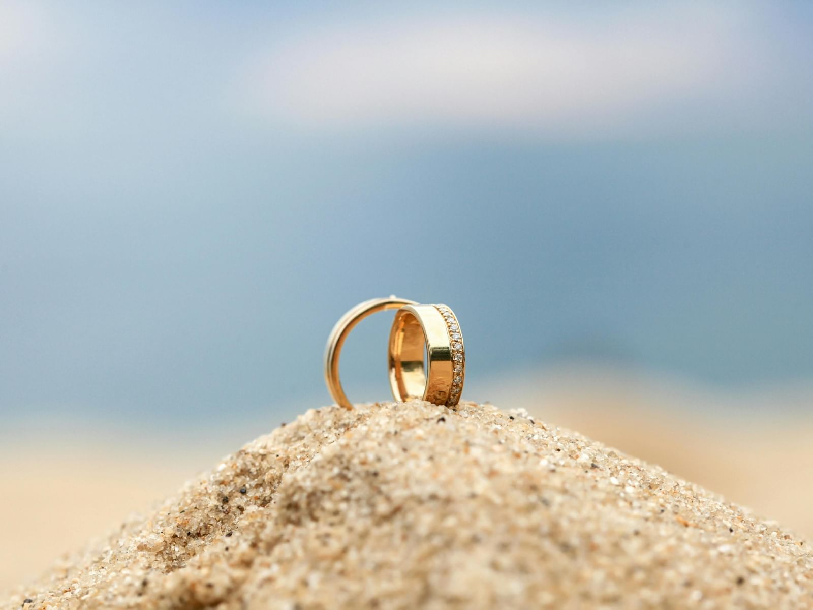 Two golden rings placed on top of a small sand mound.