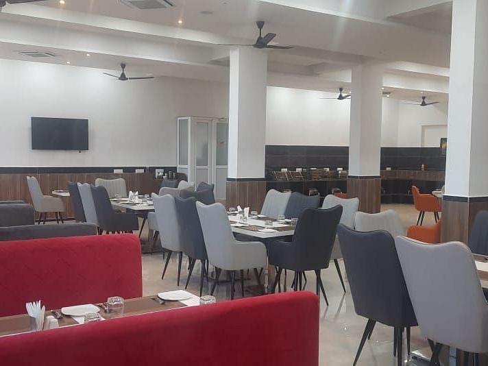 A brightly lit dining area features tables with red bench seating and grey chairs - Kankidham Lords Inn
