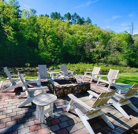 an outdoor seating area with a fire pit in the middle surrounded by wooden chairs amidst lush greenery - Historic Tapoco Lodge