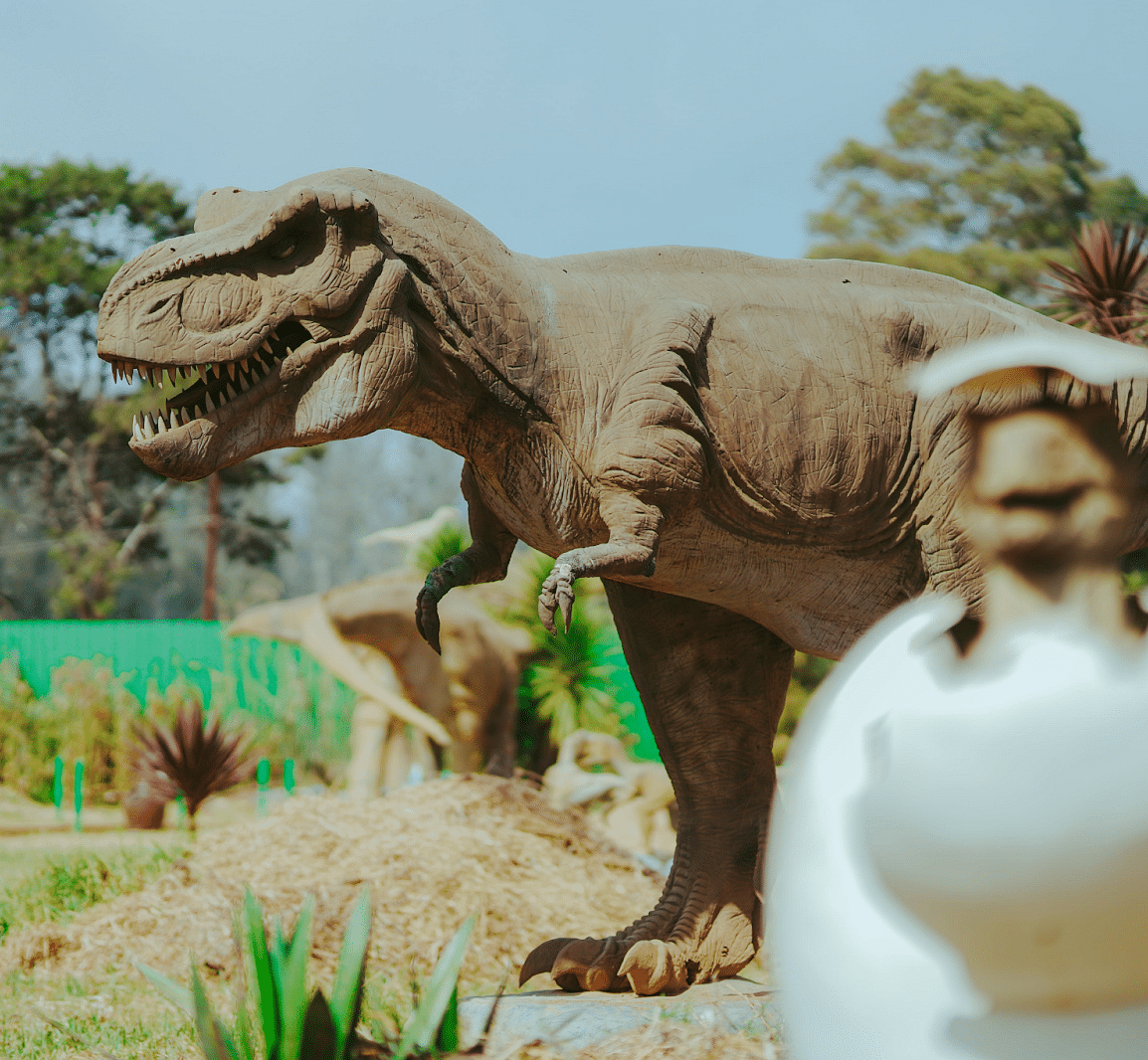 A dinosaur statue in a barren group with few shrubs around 