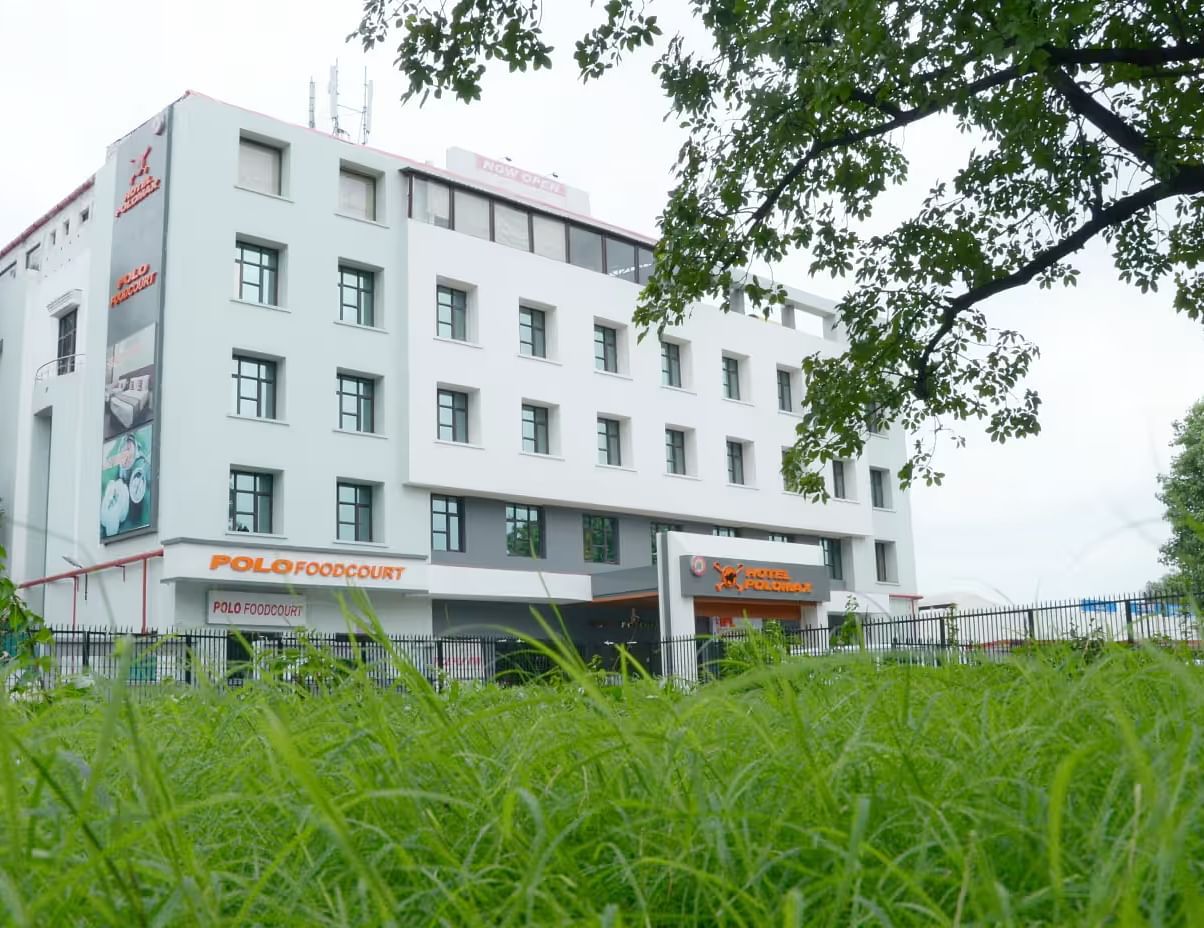Facade view of Max Hotel Prayagraj with lush green garden in the front and clear sky in the background.