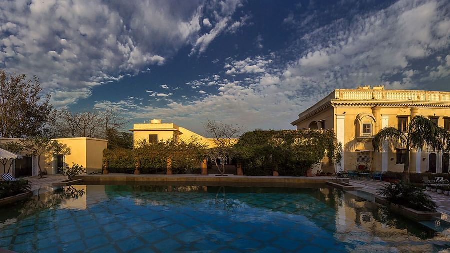  An outdoor scene featuring a pool reflecting the sky and buildings of Royal Heritage Haveli under a dramatic cloud formation.