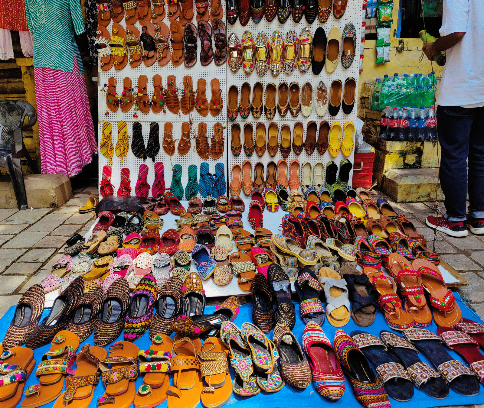 An outdoor stall displays various footwear arranged on the ground and on a shelf for sale.