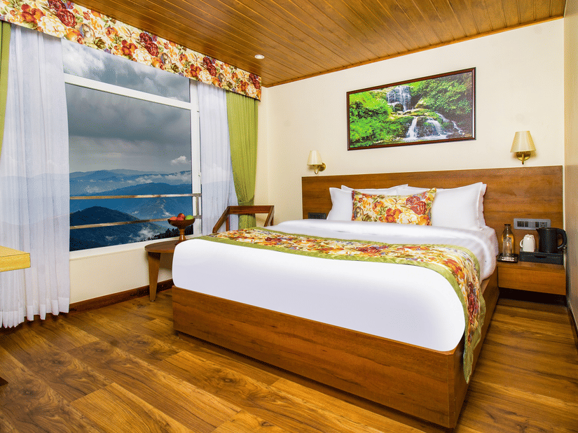 Deluxe Room featuring wooden interiors, king size bed, large window with views of hills, and cosy seating making it one of the best places to stay in Darjeeling | Mount Lungta Boutique Hotel & Spa