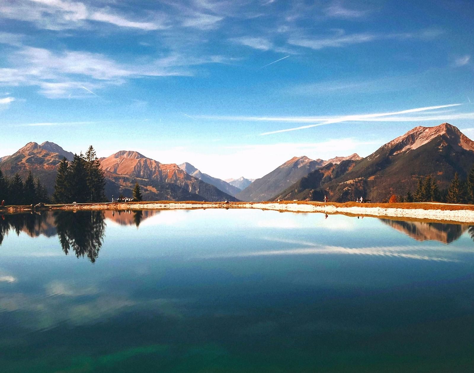 A serene mountain landscape featuring a reflective lake surrounded by towering peaks and lush trees.