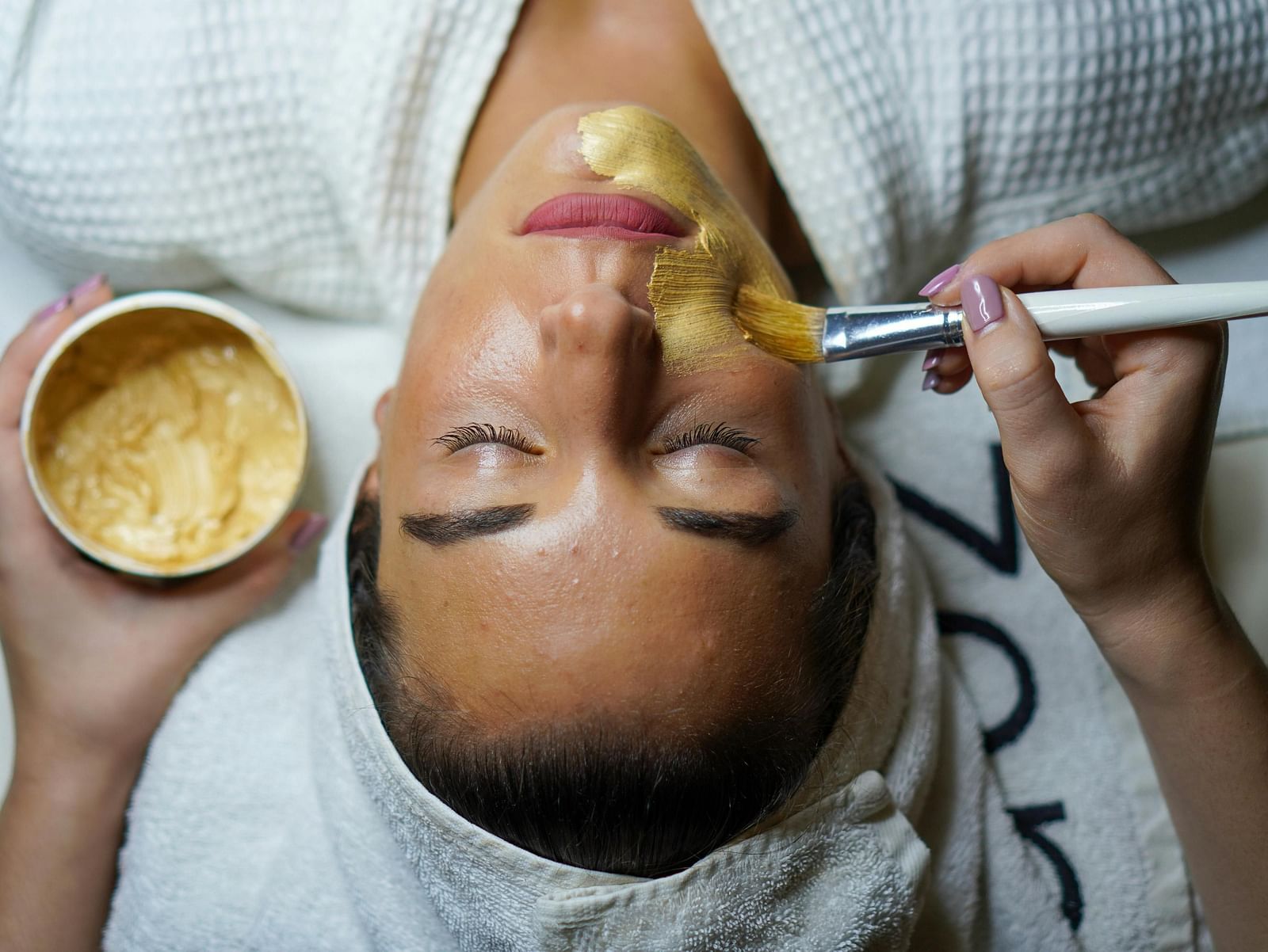 A person receiving a facial treatment with a yellow mask being applied.