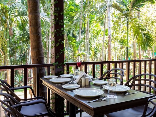 A dining table with plates and cutlery placed on it in an open air restaurant - Stone Wood Nature Resort, Gokarna