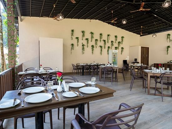 An open air restaurant with wooden tables and chairs, neatly arranged plates and cutlery and a wall with plants mounted on it - Stone Wood Nature Resort, Gokarna