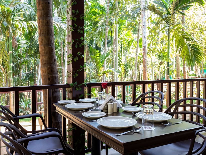 A dining table with plates and cutlery placed on it in an open air restaurant - Stone Wood Nature Resort, Gokarna