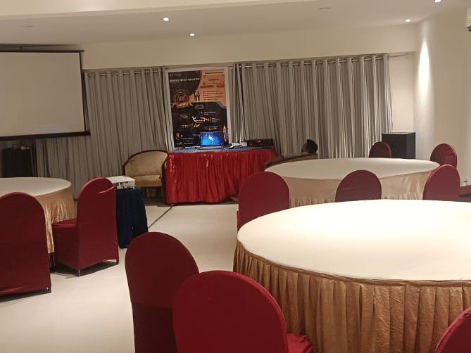 Professional banquet hall at Lords Eco Inn Dahej with round tables, burgundy chairs, and presentation screen for events and conferences