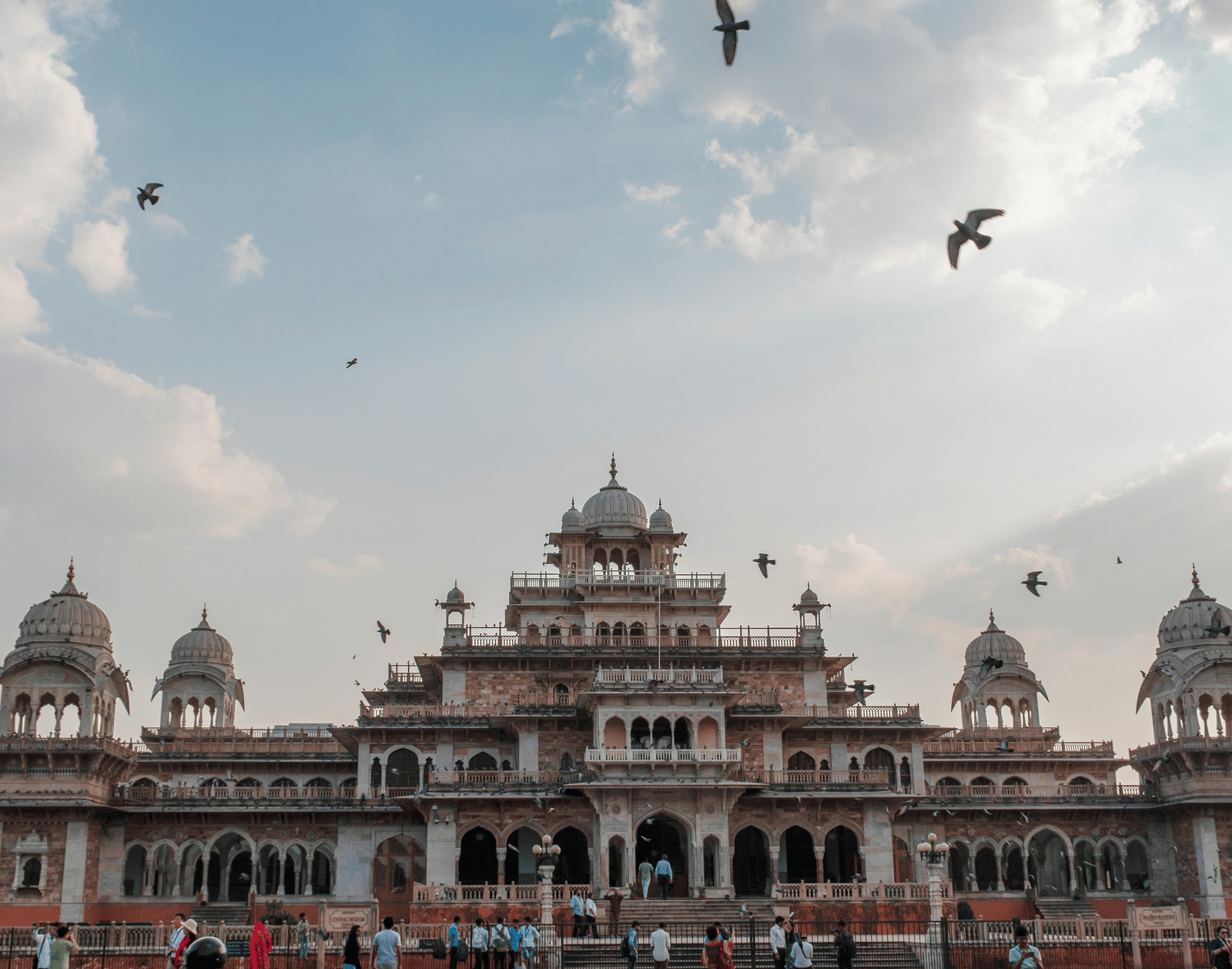 The majestic Albert Hall Museum with pigeons flying above and clear blue sky behind - Jaipur tour itinerary.