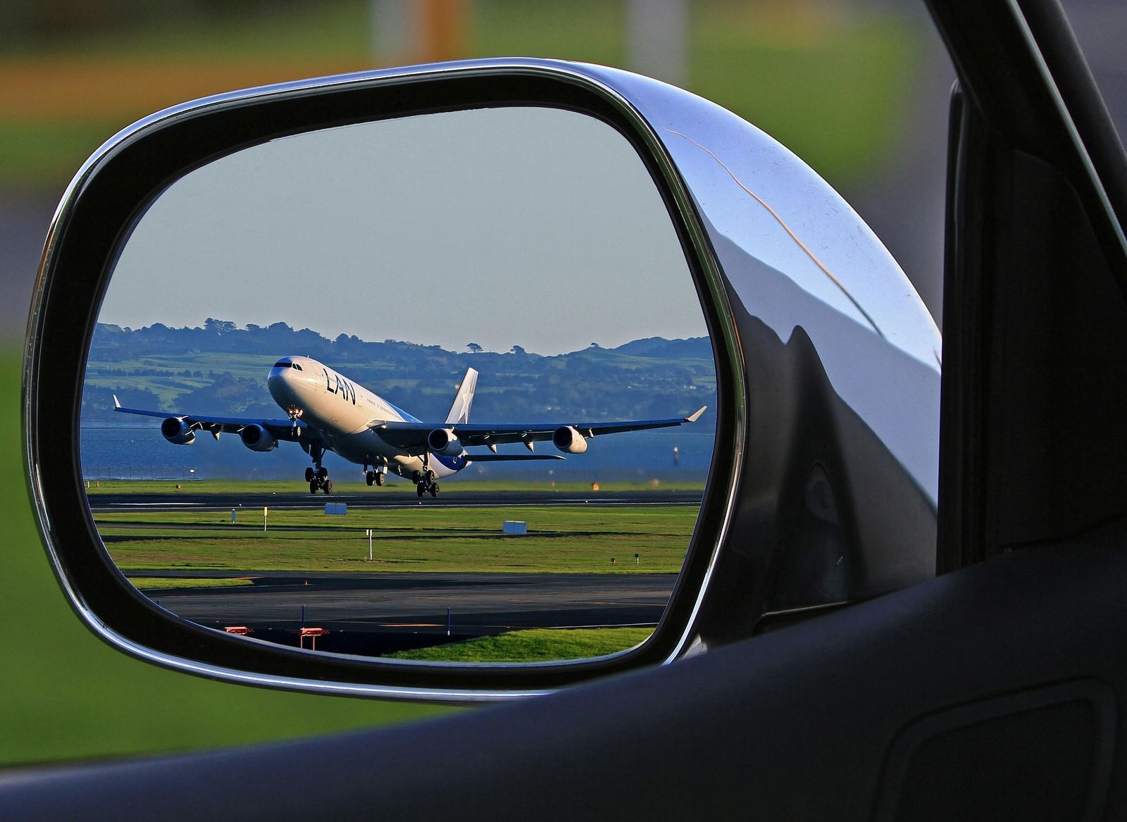 An air plane reflected in a car's side mirror, indicating close airport proximity.