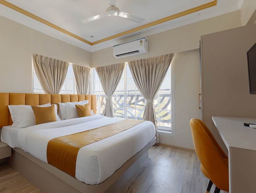 A bedroom at Home2 Residency, Mumbai Airport with large windows, light brown curtains, and a work desk.