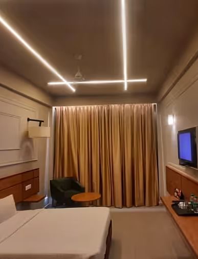 View of a modern hotel room with ambient lighting, a comfortable bed, and a wall-mounted TV - Max Hotel Prayagraj.