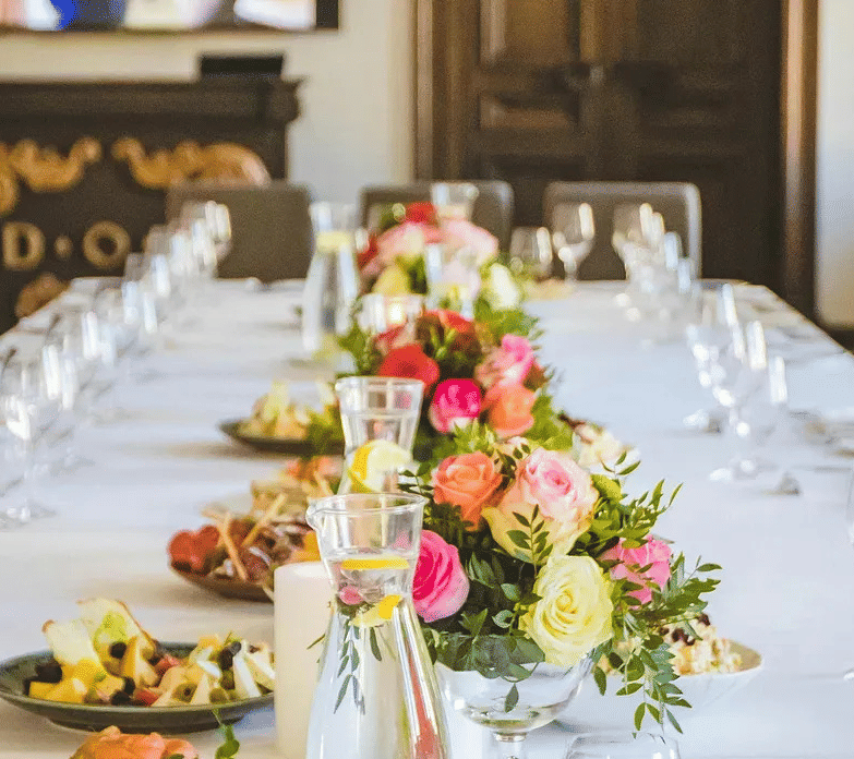 A banquet table set with white linen, flowers, and glassware, prepared for dining or an event.