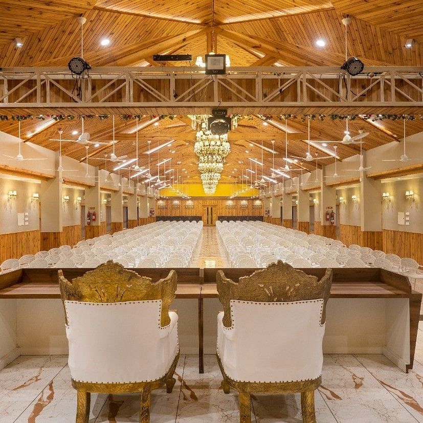 A large banquet hall with a stage area, speakers, and seating at the rear of Angel Lords Eco Inn Amreli.