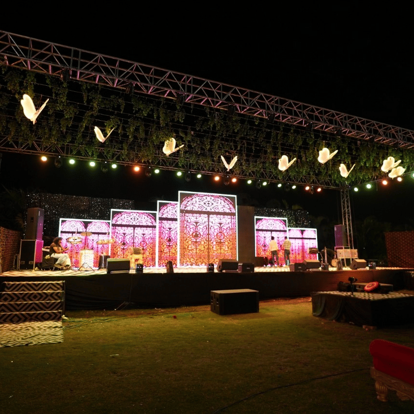 A vibrant platform setup illuminated by several overhead lights having adequate seating arrangements, and a staircase visible at the front at Gulmohar Garden of Papaya Tree Hotels.