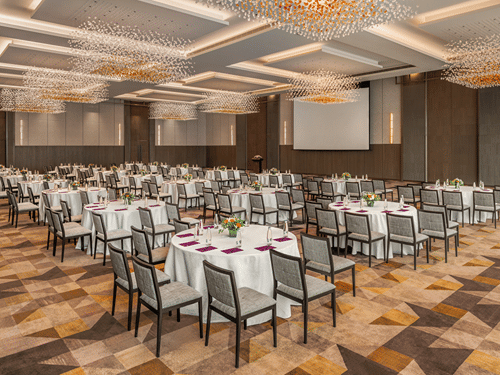An expansive banquet hall of Ballroom 1 arranged in a conference setup featuring round dining tables with white tablecloths under geometric illuminated ceiling panels at The Residency Towers Chennai.