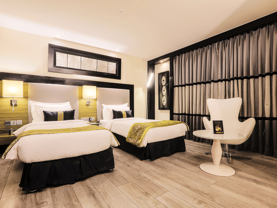 Executive Twin Room at The Empresa Hotel featuring two similar looking bed, and a chair with centre table.