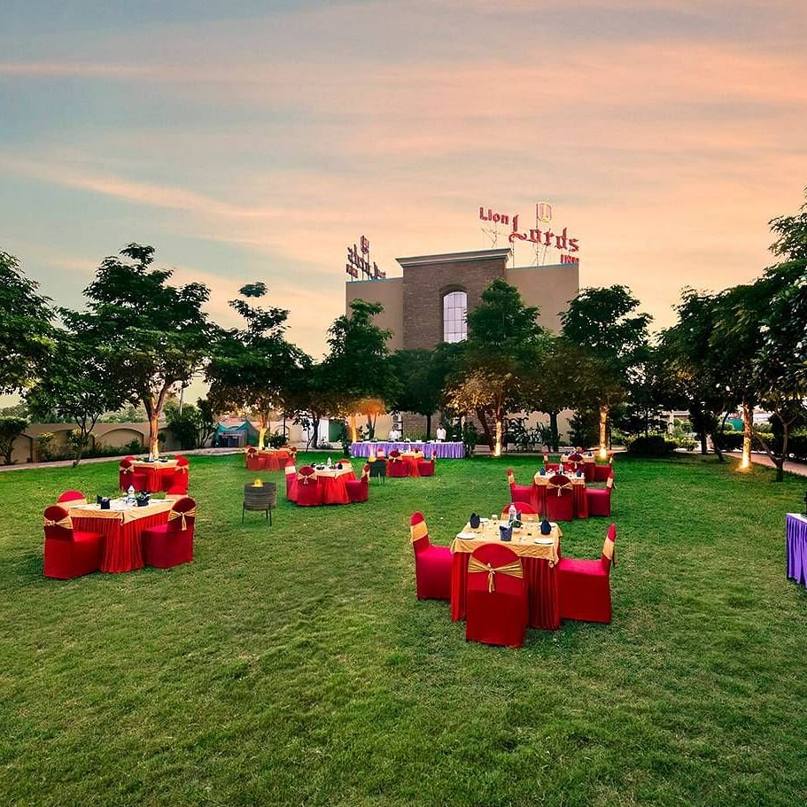An outdoor area is prepared for an event with tables covered in red cloths on the grass - Lion Lords Inn Rajula