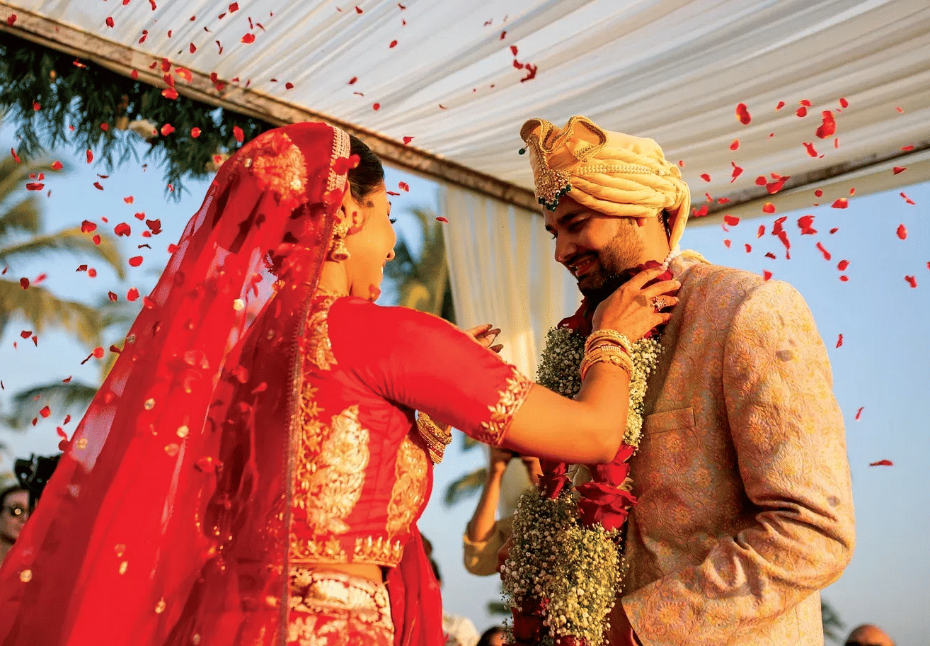 Indian bride and groom exchanging garlands amid rose petals during beachside wedding ceremony at Caravela Beach Resort Goa