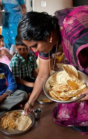 People eating from plates on the floor, indoor setting - Shreyas Retreat