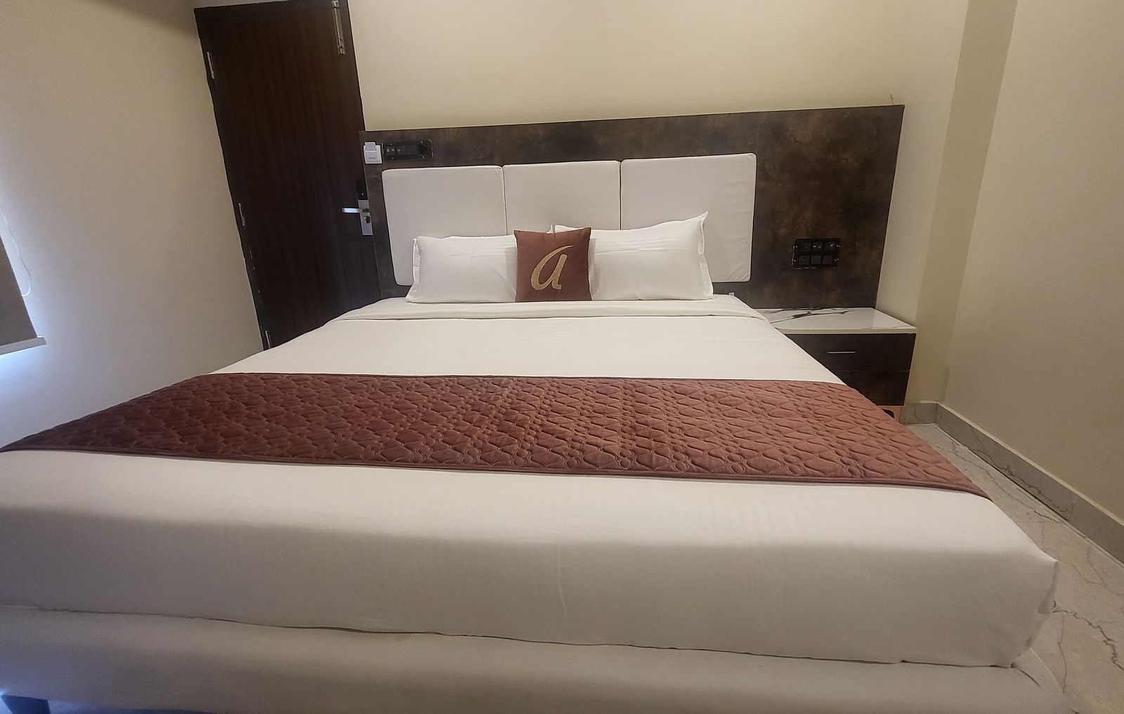 A simple and modern hotel room featuring a comfortable double bed with white linens and a decorative brown cushion - Astra Hotels and Suites, HSR Sector 7