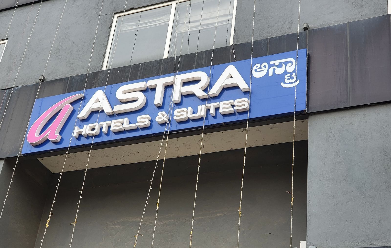 The exterior signage of Astra Hotels & Suites, a modern black building with a bold blue and red sign - Astra Hotels & Suites, Sarjapura
