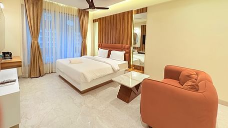 A spacious bedroom featuring a king size bed, a large sofa, and a wall-mounted television at Hotel Mumbai House, Vashi