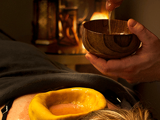 A hand holding a container with liquid over the back of a person with a dough ring at YO1 Longevity & Health Resorts