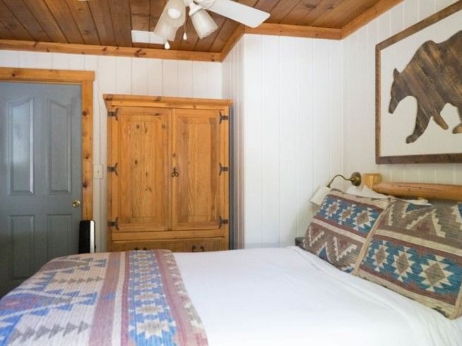 a wooden armoire, patterned pillows on a bed, a bear silhouette artwork, and a grey door in a Room at Shaver Lake Village Hotel.