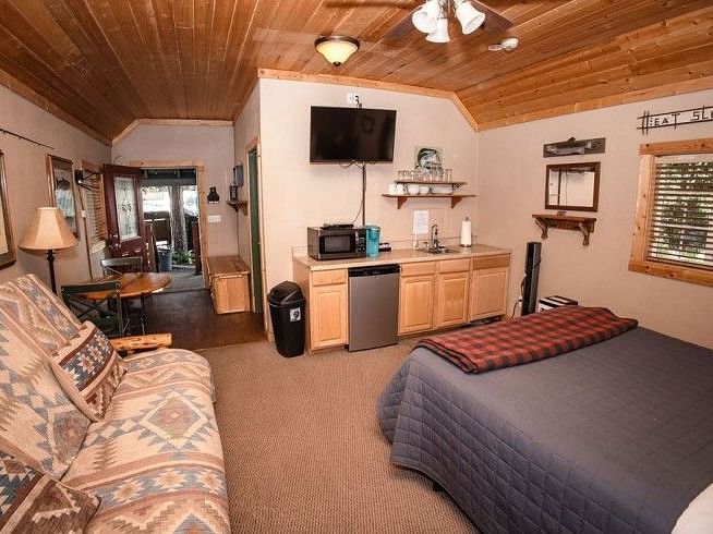 a Room with a bed, couch, TV, kitchenette, wood ceiling, and an open doorway to another room at Shaver Lake Village Hotel.