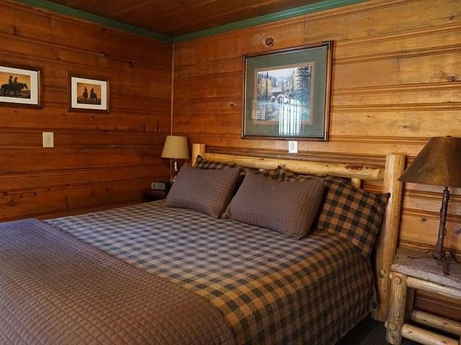 a Bedroom at Shaver Lake Village Hotel with a wooden bed frame, plaid bedding, wood paneled walls, and framed artwork.