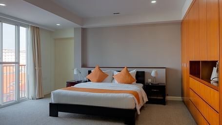 A bedroom with a bed, bedside tables, and an orange accent wall | Penthouse | Central Mansions, Phnom Penh