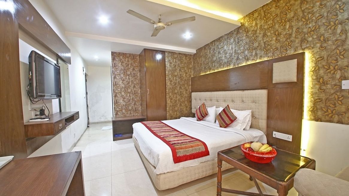 A hotel room with a textured accent wall, a plush bed with decorative pillows, a wooden table, and a TV, illuminated by warm ceiling lights. - Hotel Diamond Plaza, Chandigarh.